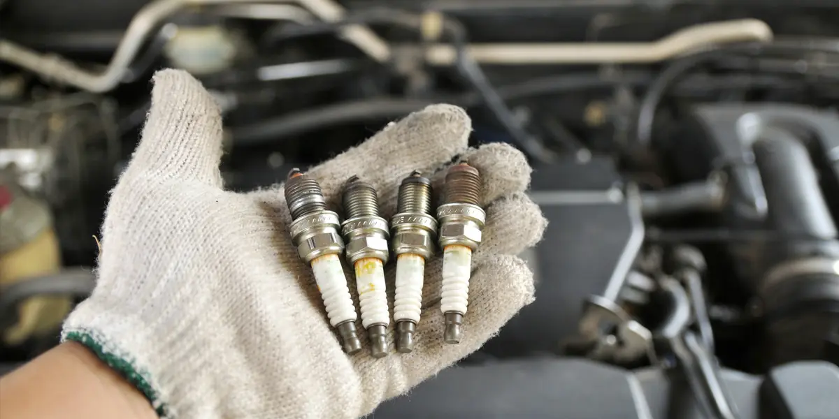 Eldivenli elinde motordan sökülmüş dört kullanılmış buji tutan usta