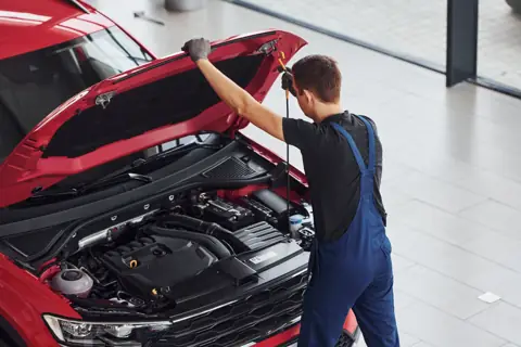 Servis çalışanı, kaputu açık kırmızı bir aracın motor yağı seviyesini çubukla kontrol ediyor