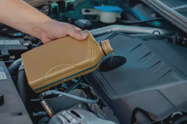 Motor bölmesinde yağ bidonunu dolum ağzına doğru eğen bir el